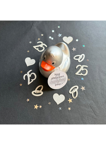 “Zilverkleurige badeend met hangtag ‘Nog altijd een spetterend paar!’, omringd door confetti voor 25 jaar huwelijk.”