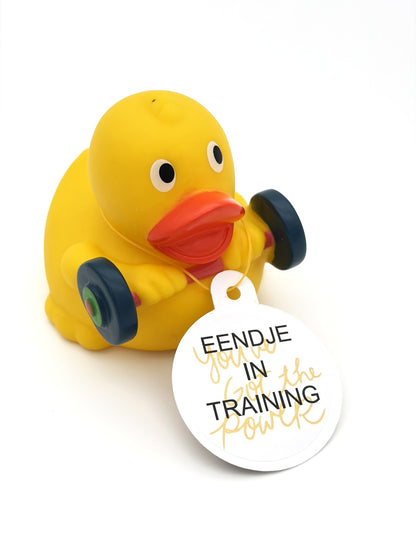 Gele fitnessbadeend met oranje snavel, halter en een witte hangtag met de tekst ‘Eendje in training’ en ‘You have the power’.