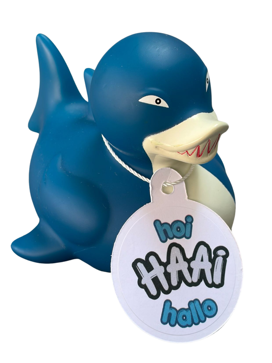 Blauwe haaibadeend met witte buik, scherpe tandjes en een hangtag met de tekst ‘Hoi Haai Hallo’.