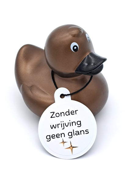 Bronskleurige badeend met zwarte snavel en een witte hangtag met twee fonkelende sterren en de tekst ‘Zonder wrijving geen glans’.