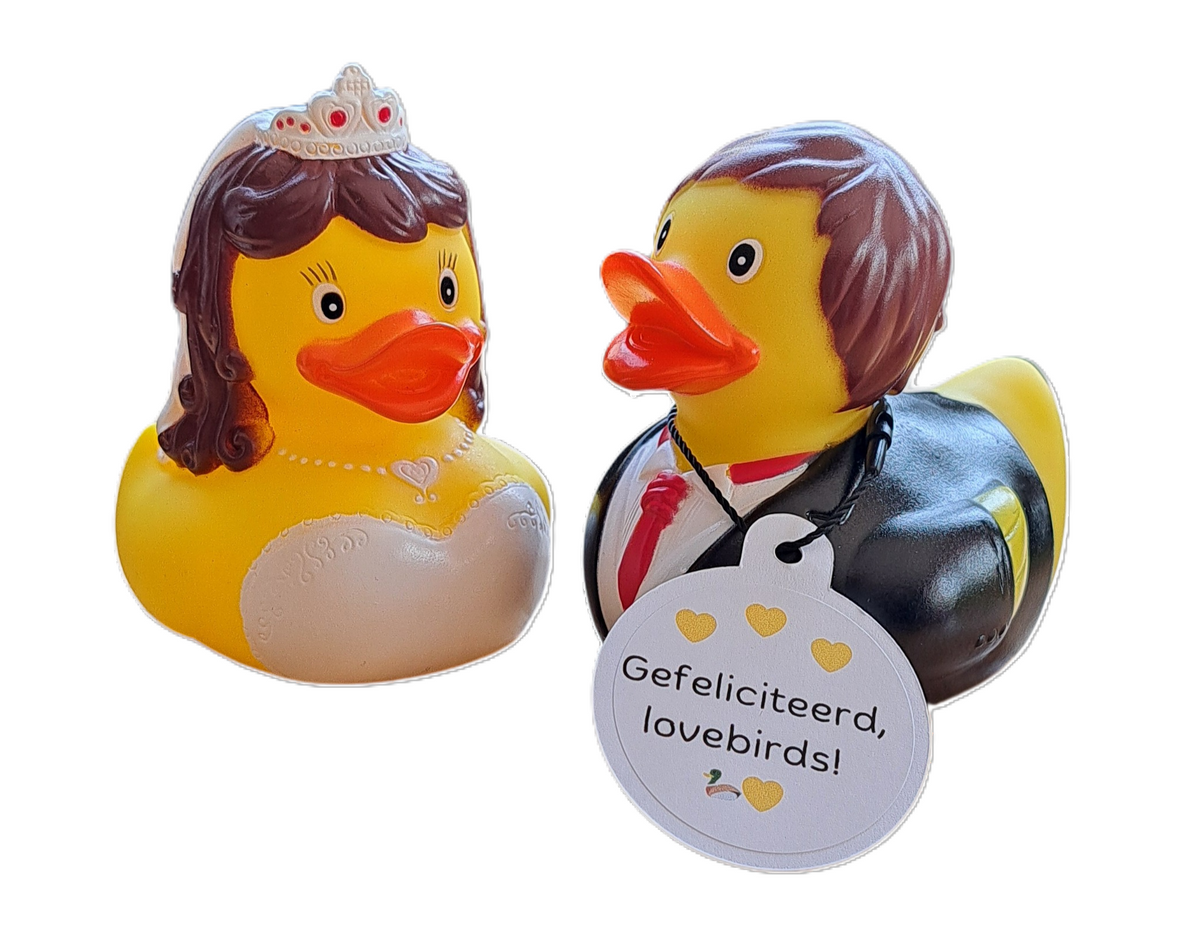 Badeend-bruidspaar met een bruid in witte jurk en tiara en een bruidegom in zwart pak met rode stropdas, met een witte hangtag ‘Gefeliciteerd, lovebirds!’.
