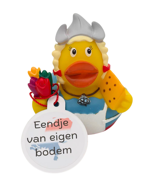Gele badeend in Hollandse klederdracht met blonde vlechten, witte kap, tulpen en een stuk kaas, met een hangtag ‘Eendje van eigen bodem’.