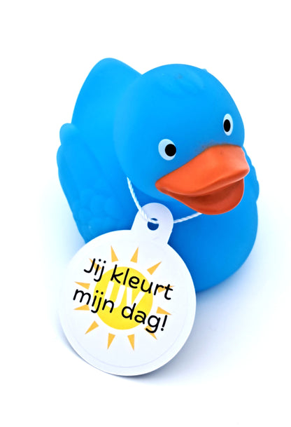 Blauwe badeend met oranje snavel en een witte hangtag met een geel zonnetje en de tekst ‘Jij kleurt mijn dag!’.