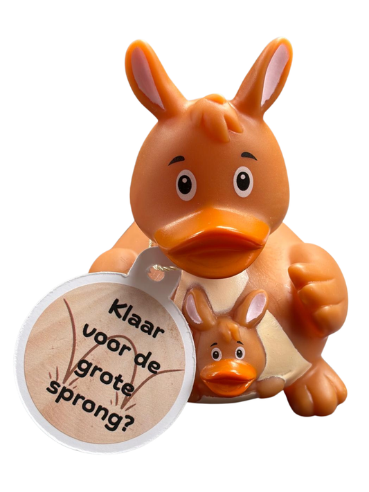 Bruine kangoeroebadeend met een kleintje in de buidel en een hangtag met de tekst ‘Klaar voor de grote sprong?’.”
