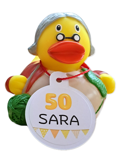 Gele Sara-badeend met grijs haar, ronde bril en groen breiwerk, met een kaartje ‘50 SARA’ voor haar 50e verjaardag.